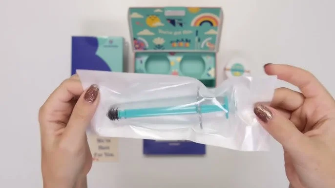 hands holding a teal syringe in packaging, with a colorful kit box and other items in the background