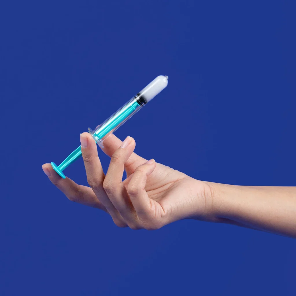 hand holding a syringe with a blue plunger against a solid blue background